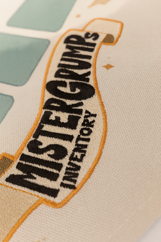 Close-up of embroidered detail showing Mr. Grumps characters and autumn items on canvas banner