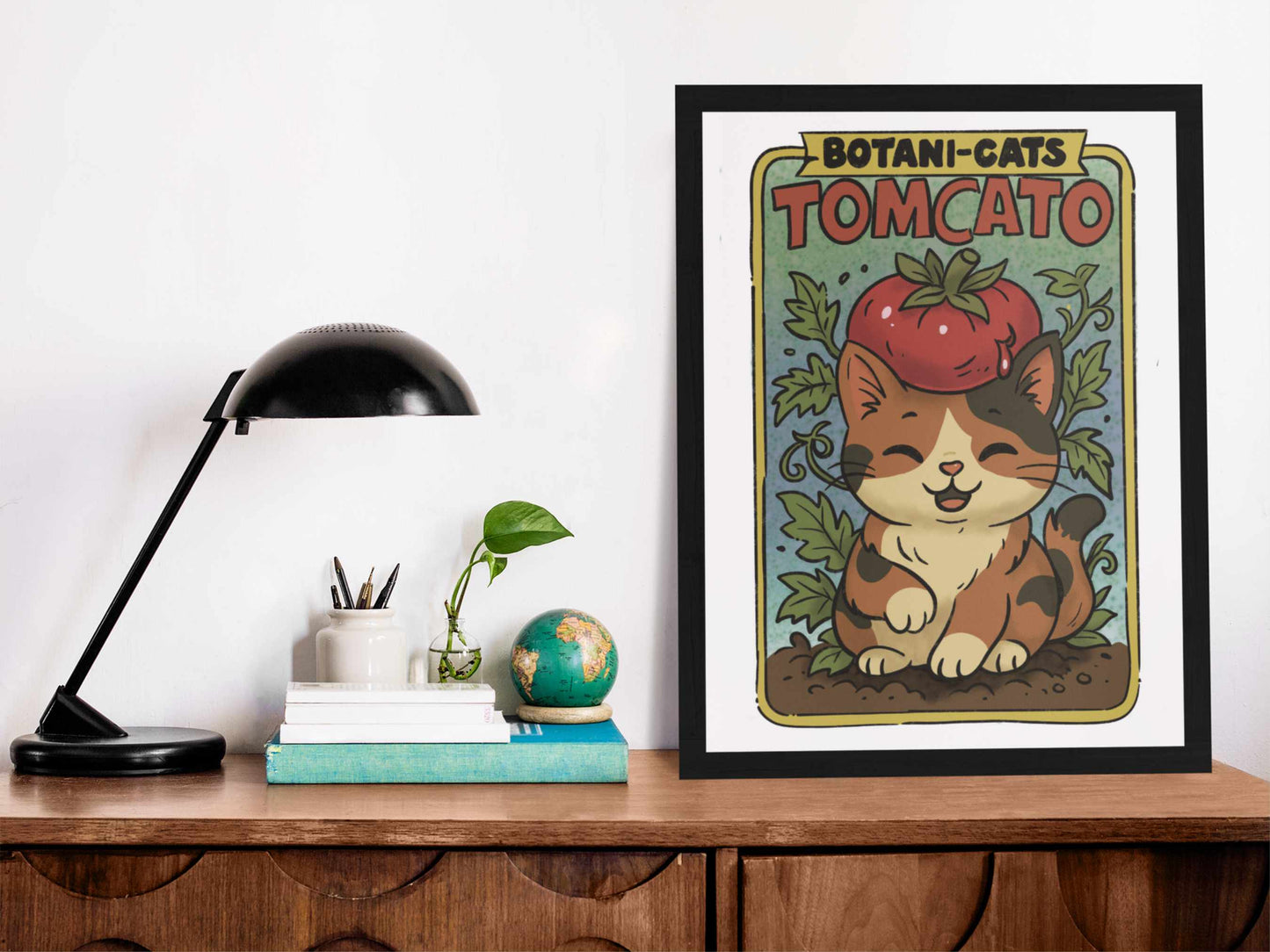 Tomcato art print framed and displayed on a wooden desk with books, a globe, and a lamp – whimsical tomato cat illustration in cozy decor setting