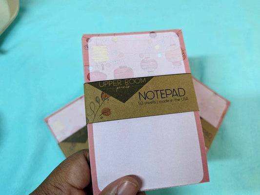Hand holding the Lunar Lantern Notepad to show size and festive pink and red lantern cover design