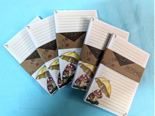 Fanned stack of Mushroom Rain Notepads with whimsical mushroom and umbrella design on 4x6 handmade pages.