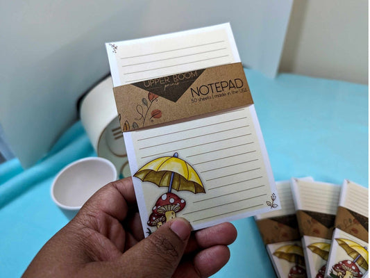 Hand holding the Mushroom Rain Notepad, showing its 4x6 size and illustrated cottagecore design.