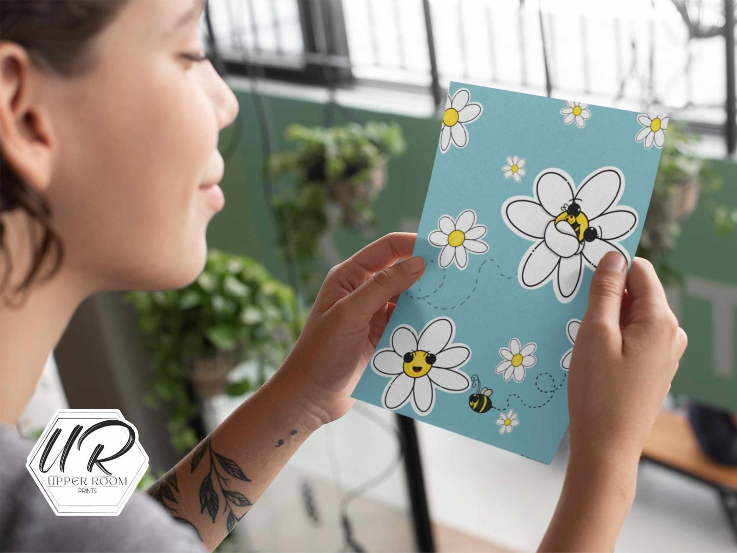 Woman holding and looking at the Summer Buzz Print, featuring a colorful bee-themed design with Rosie and Bebe