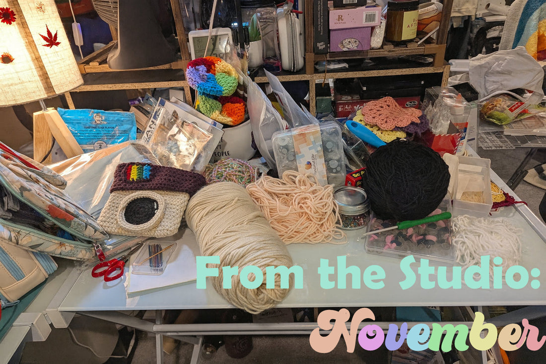 Crowded craft table in the Upper Room Prints studio covered in yarn, crochet projects, and supplies with the words “From the Studio: November” overlaid at the bottom.