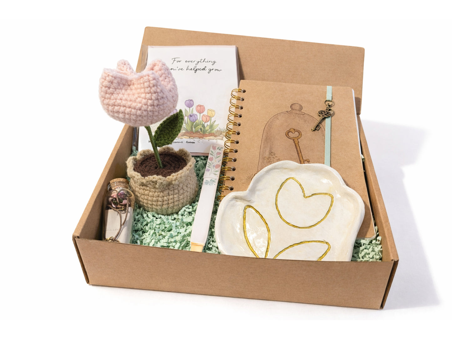 Gift box with decorative items including a plant, notebook, and heart-shaped dish on a white background