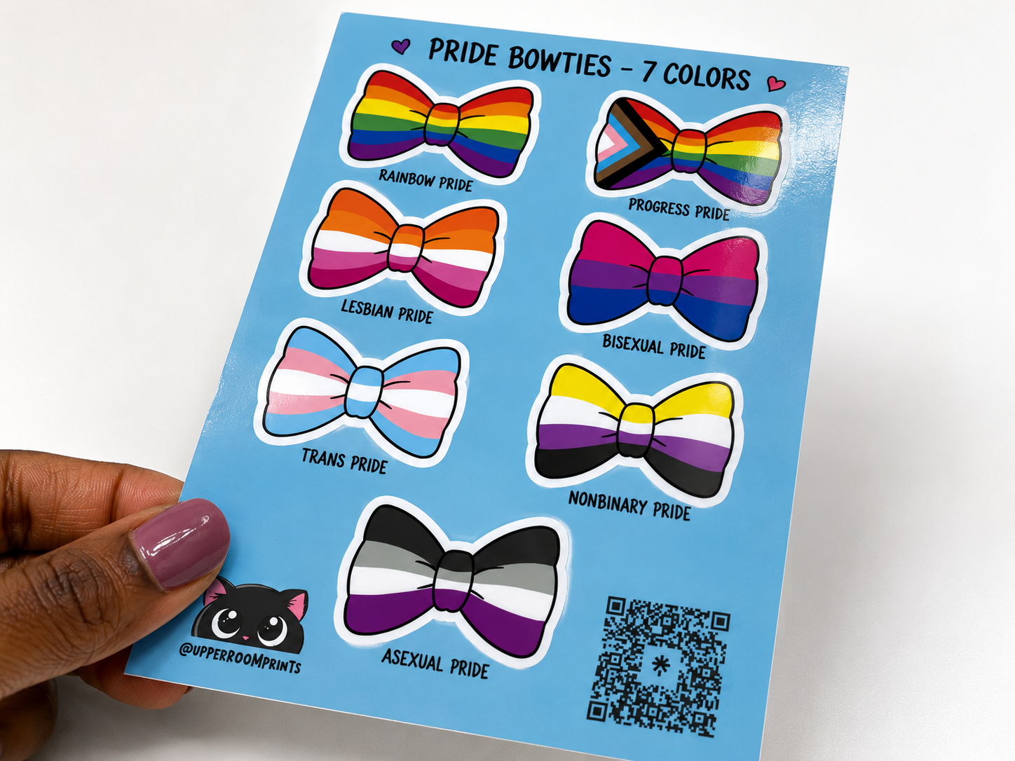 Sheet of rainbow pride bowtie stickers held by a hand with a white background