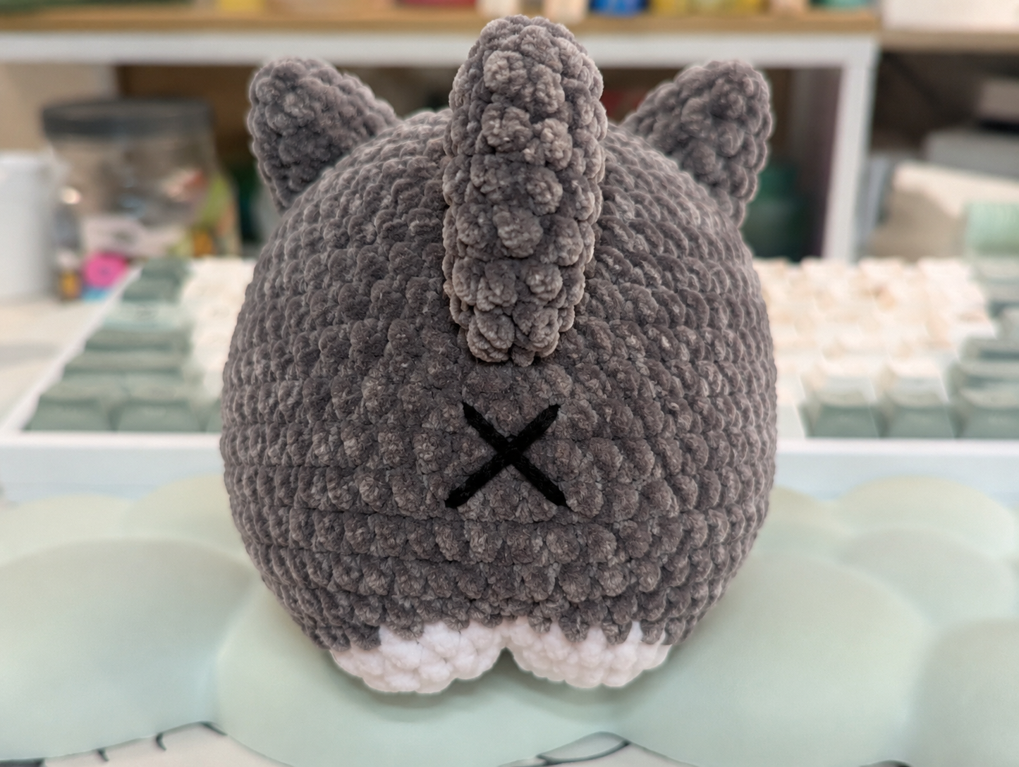 Gray knitted cat-shaped pillow on a light green surface with a blurred background