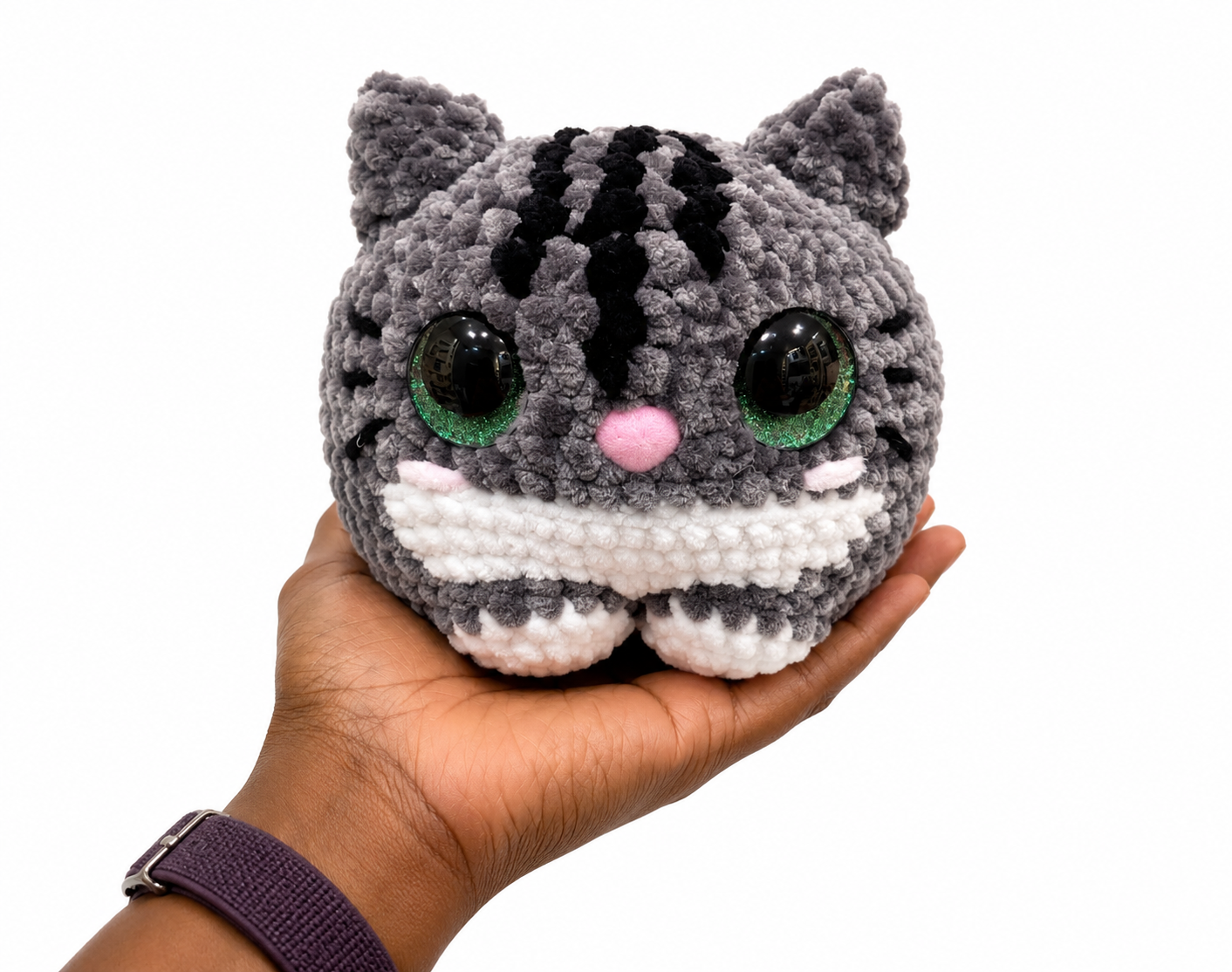 Hand holding a small crochet cat plush toy with a white background