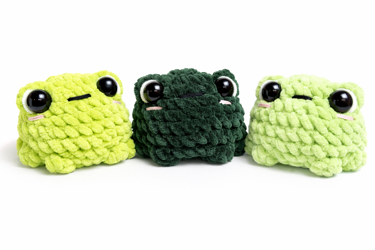 Three crochet frog plushies lined up with shiny black safety eyes in three shades of green.