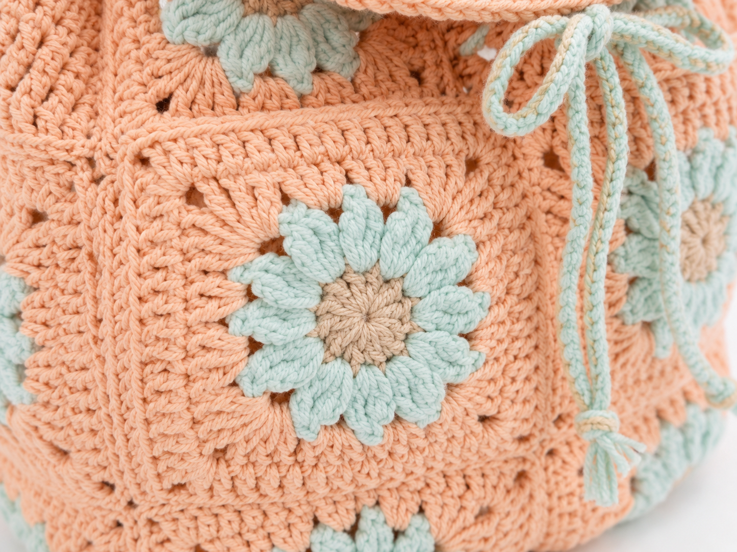 Close-up of a crocheted bag with floral patterns in peach and light blue.