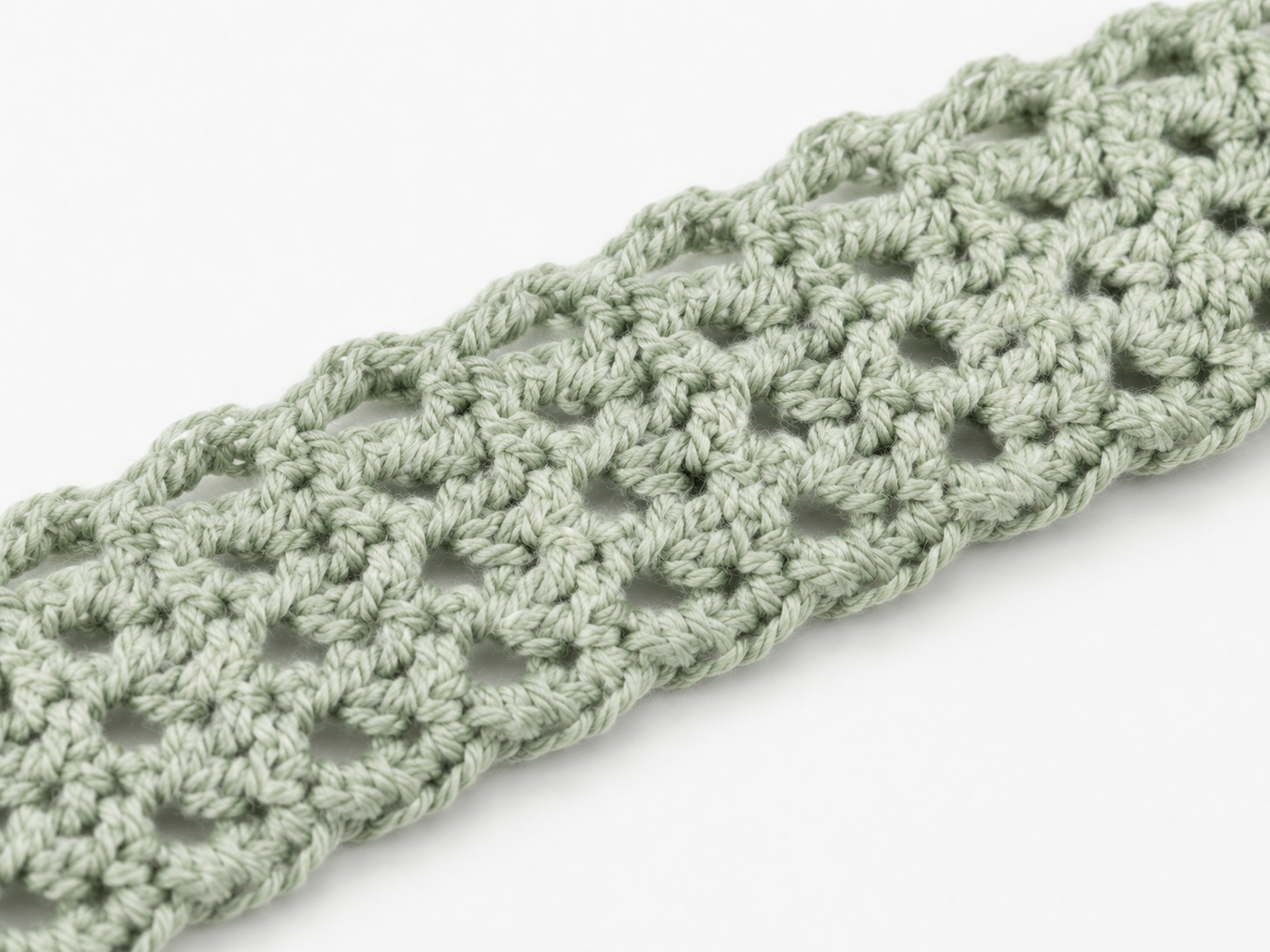 Close-up of a green crocheted headband on a white background