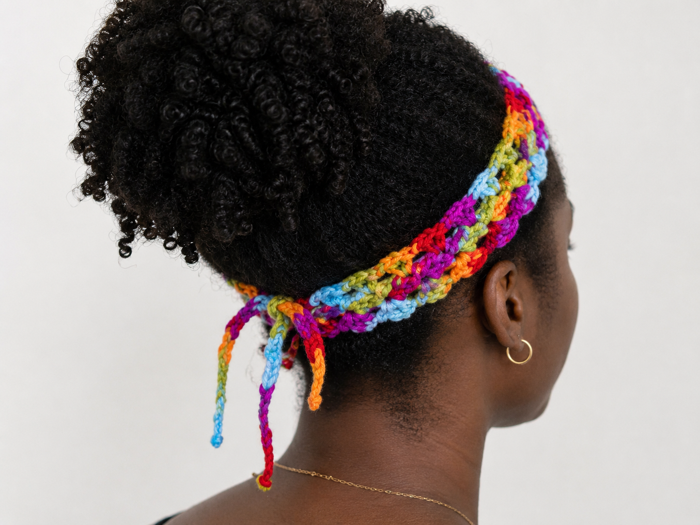 Person wearing a colorful headband with braided extensions on a plain background