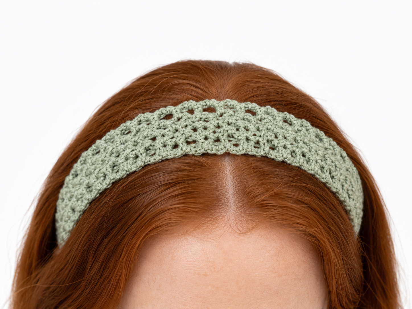 Green crochet headband worn by a person with red hair on a white background