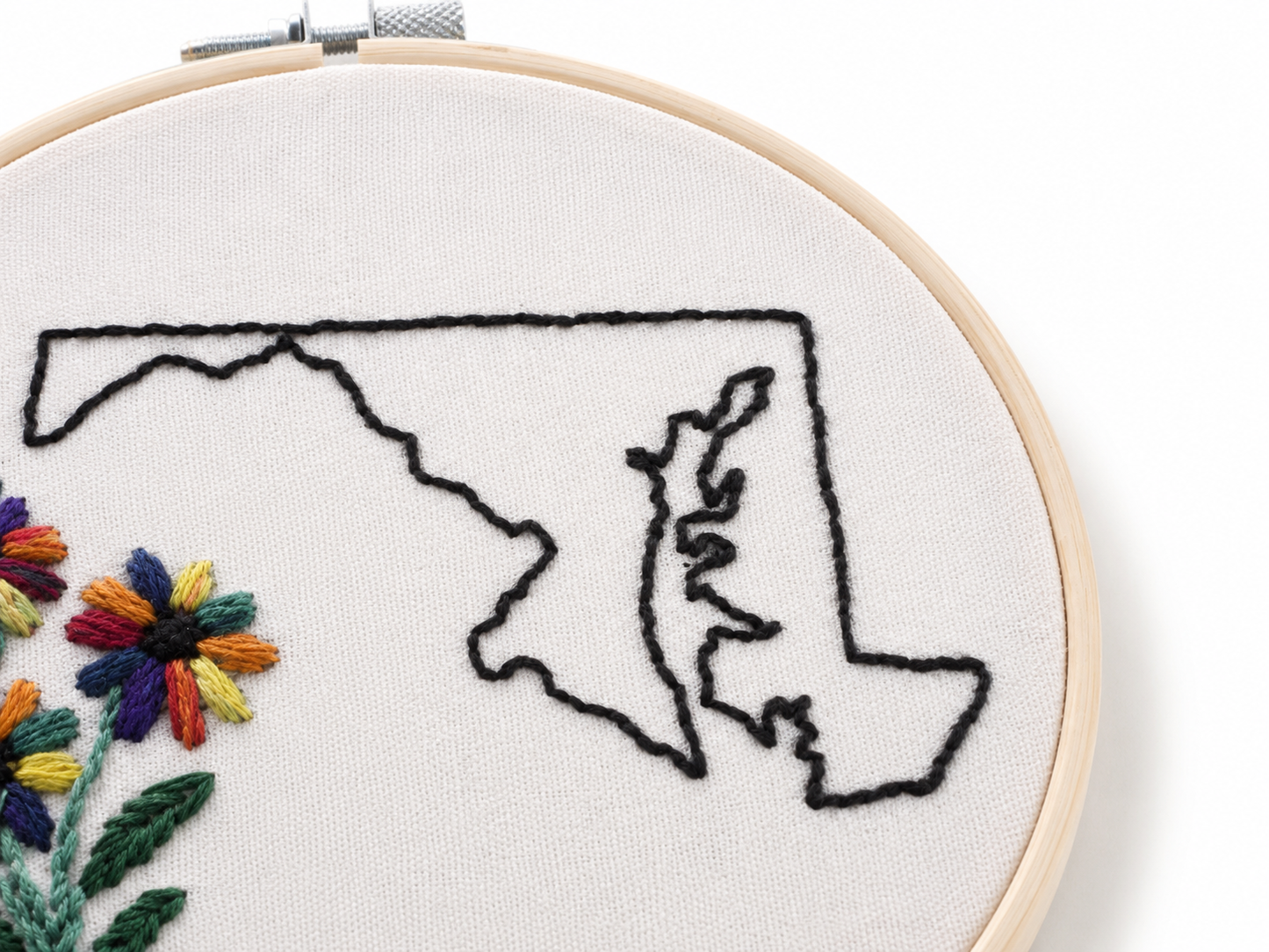Embroidery hoop with a map outline and floral details on white fabric.