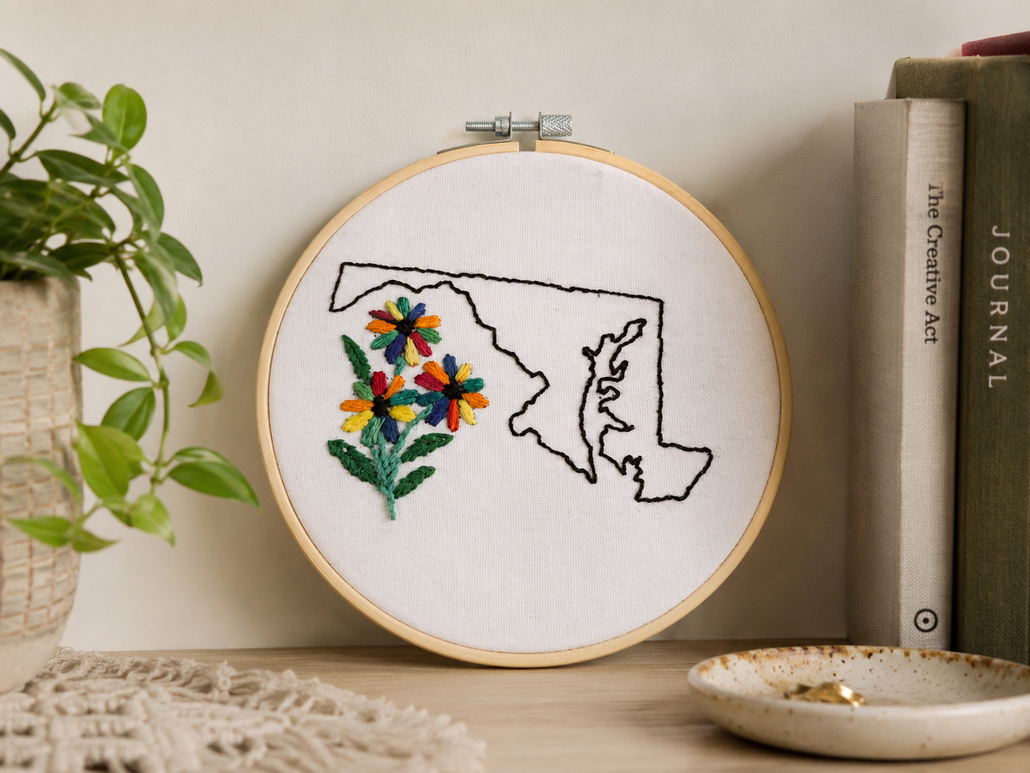 Embroidery hoop with floral design inside a map outline on a neutral background