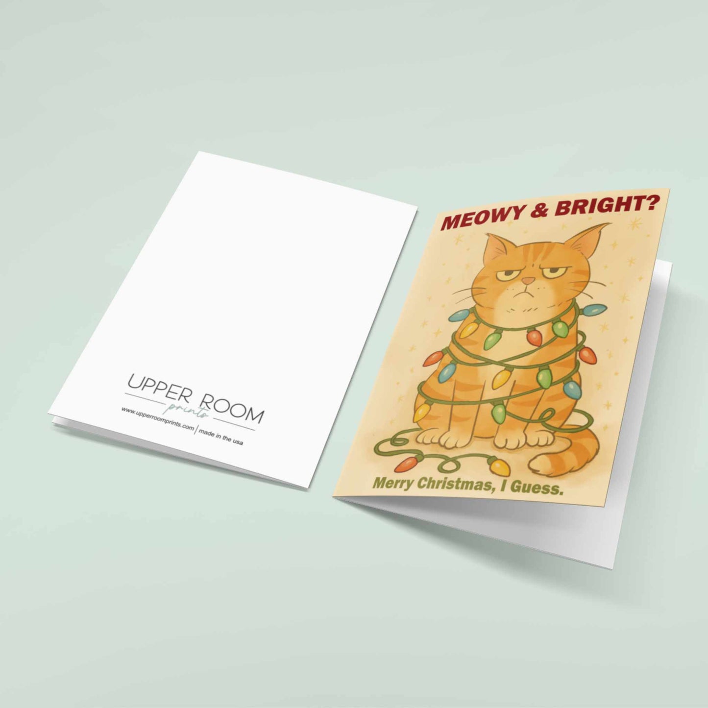 Front and back view of funny grumpy orange cat Christmas card reading "Meowy & Bright? Merry Christmas I Guess" with cat tangled in colorful holiday lights, Upper Room Prints branding on back