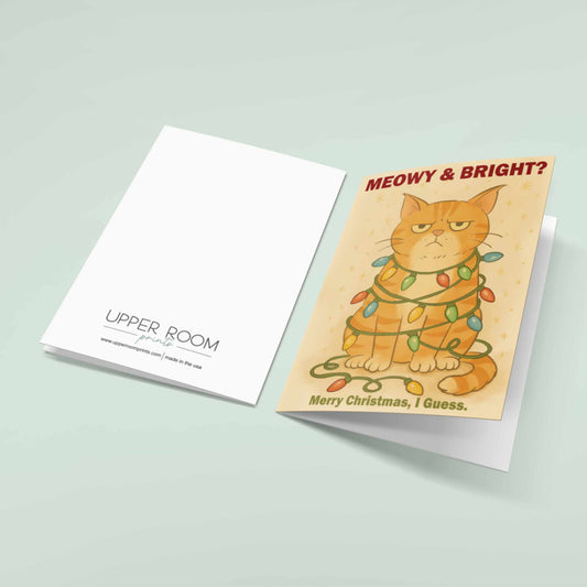 Front and back view of funny grumpy orange cat Christmas card reading "Meowy & Bright? Merry Christmas I Guess" with cat tangled in colorful holiday lights, Upper Room Prints branding on back