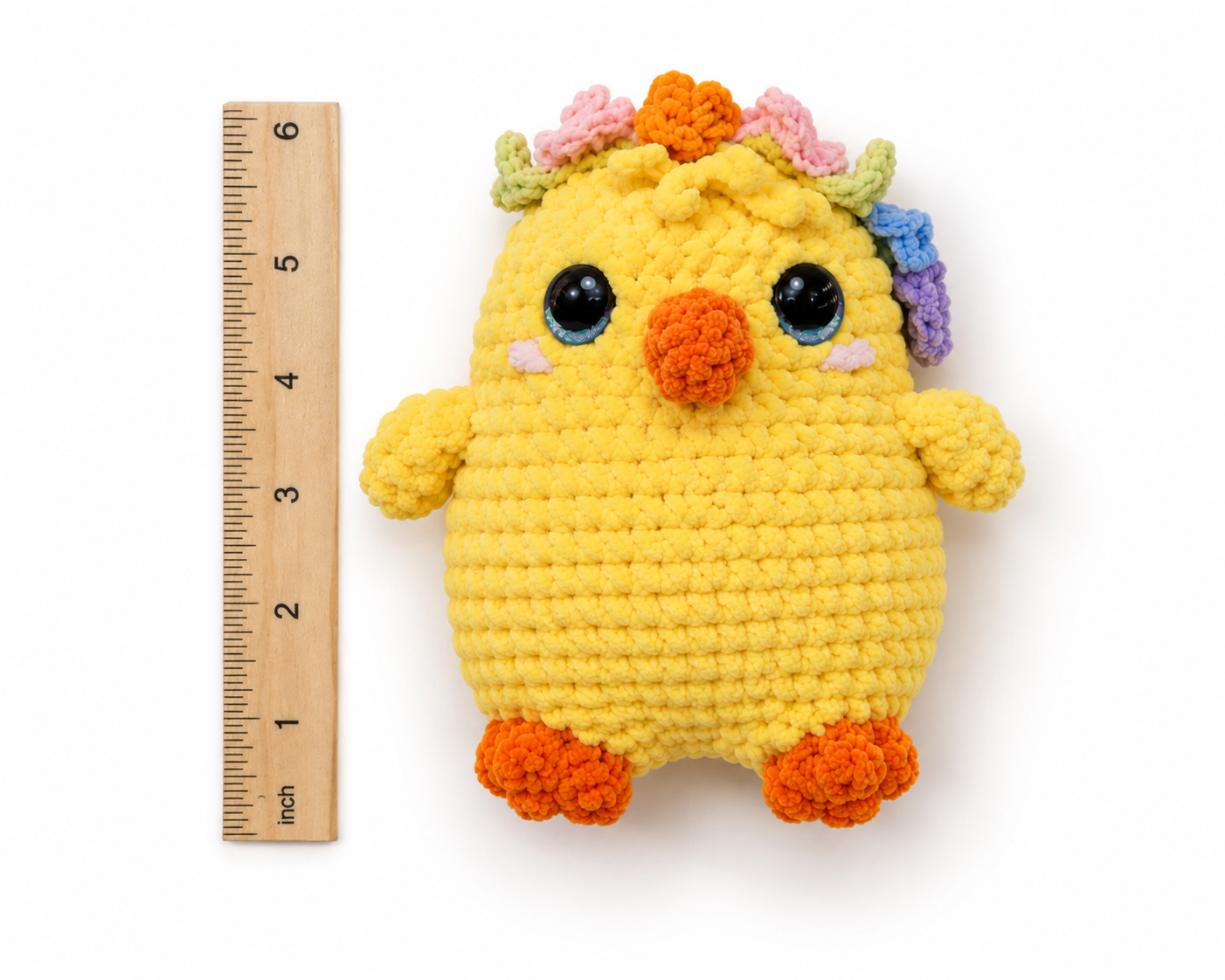 Yellow crochet toy with colorful flowers on a white background, next to a ruler for scale.
