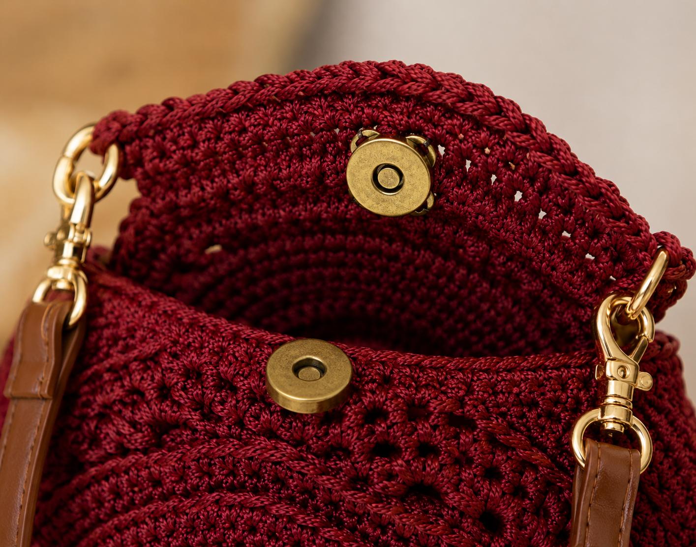 Close-up of a red crochet handbag with gold accents and brown leather straps.