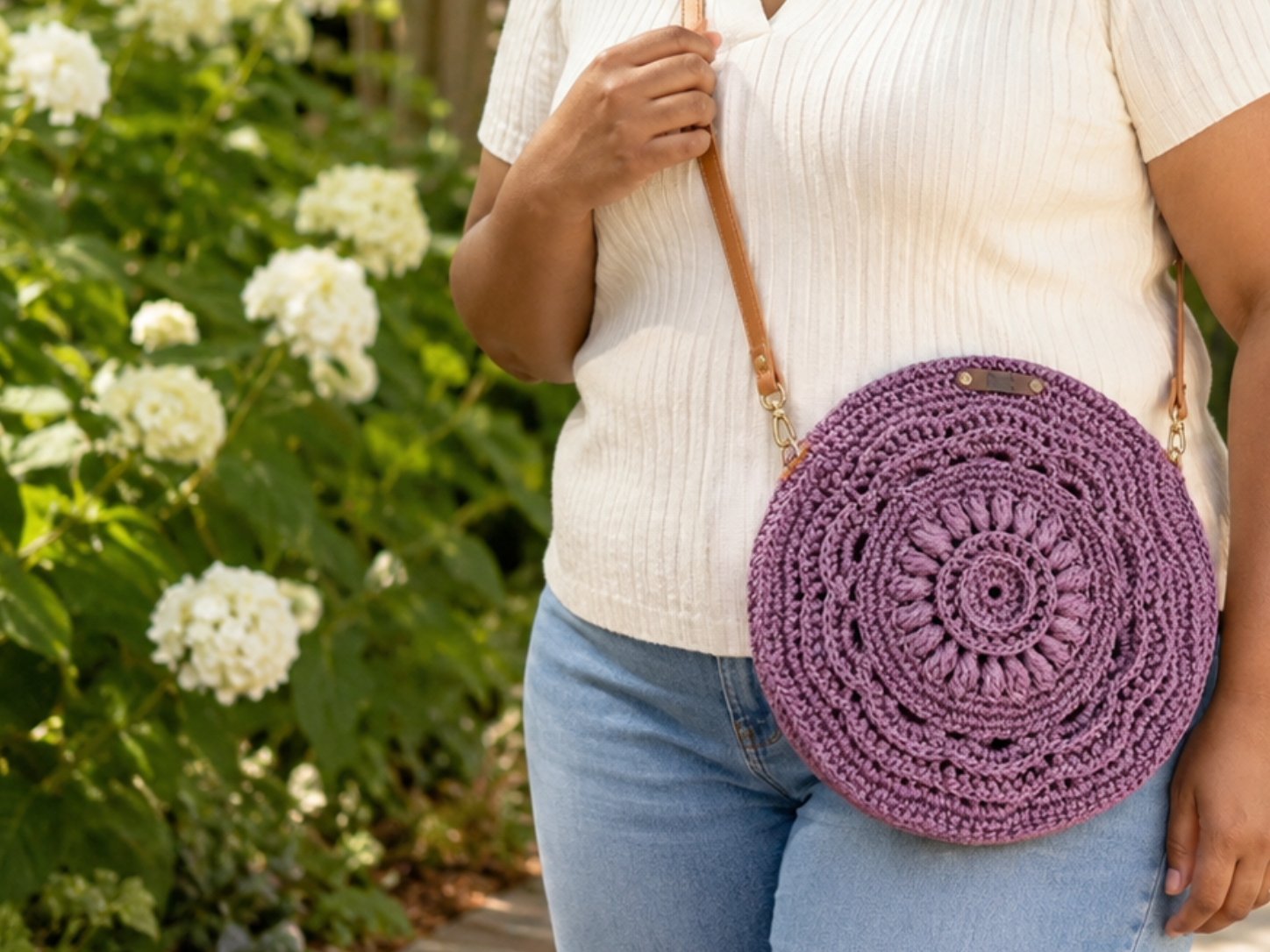 Person holding a purple crocheted bag with flowers in the background