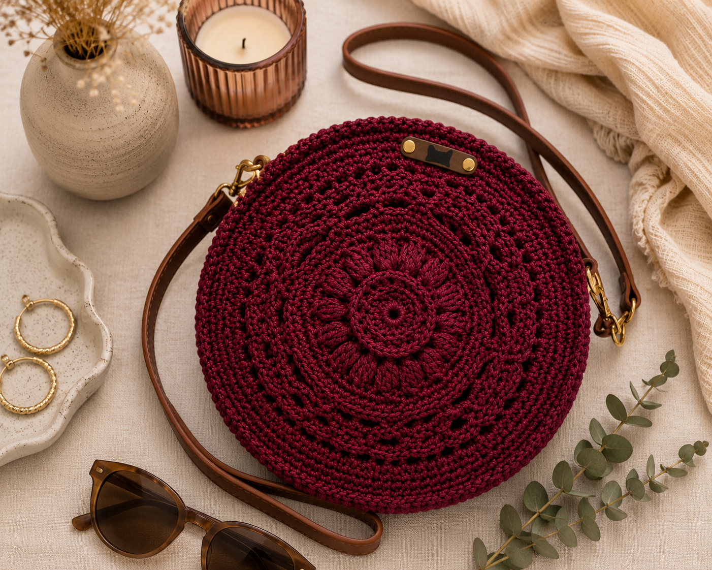 Round crochet bag with brown strap on a light surface with decorative items.