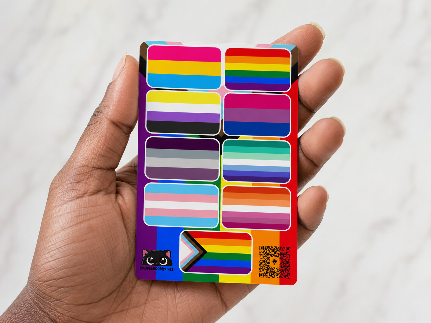 Hand holding a colorful LGBTQ+ pride flag sticker sheet against a white background