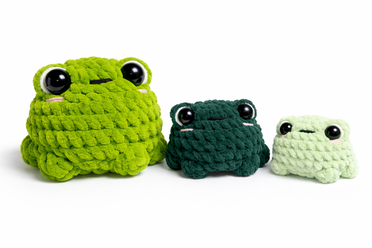 Three handmade crochet frog plushies in light green, dark green, and mint green on a white background.