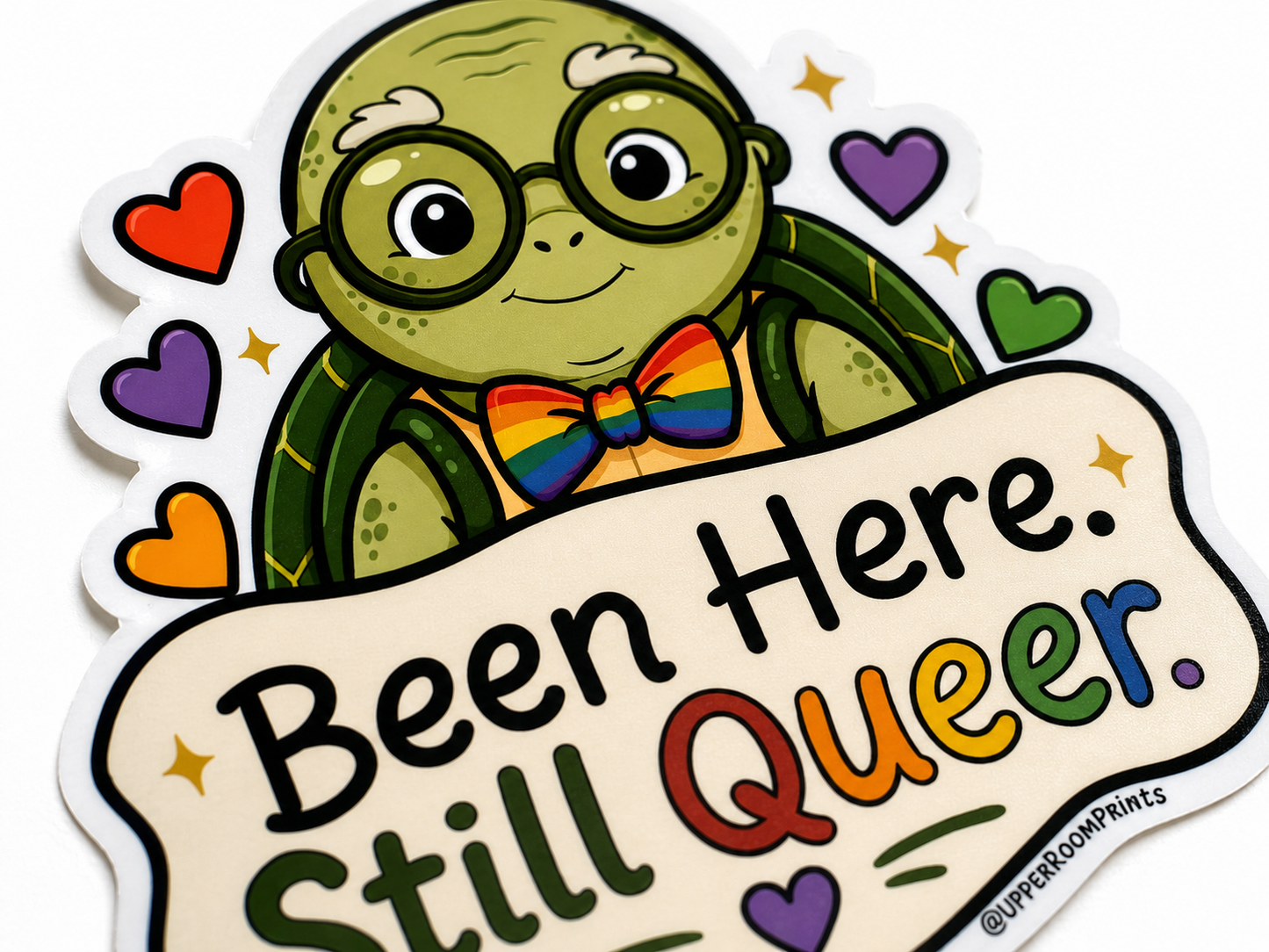 Sticker with a turtle character wearing glasses and a rainbow bow tie, holding a sign that reads 'Been Here. Still Queer.