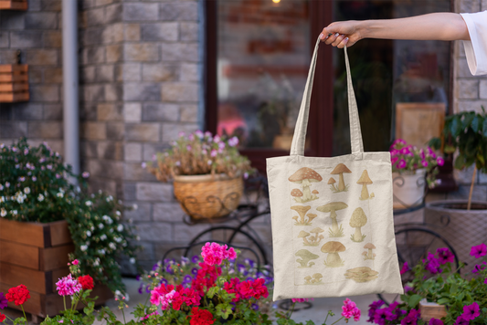 Tote bag with mushroom design held by a person outdoors with plants and flowers.