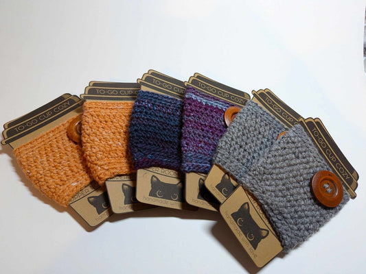 Three Cozy Sweater Drink Cozies in purple, orange, and grey arranged side by side.