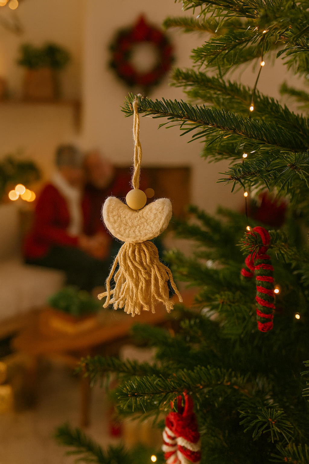 Handmade crochet angel ornament with cream wings and tassel hanging on Christmas tree with cozy holiday lights