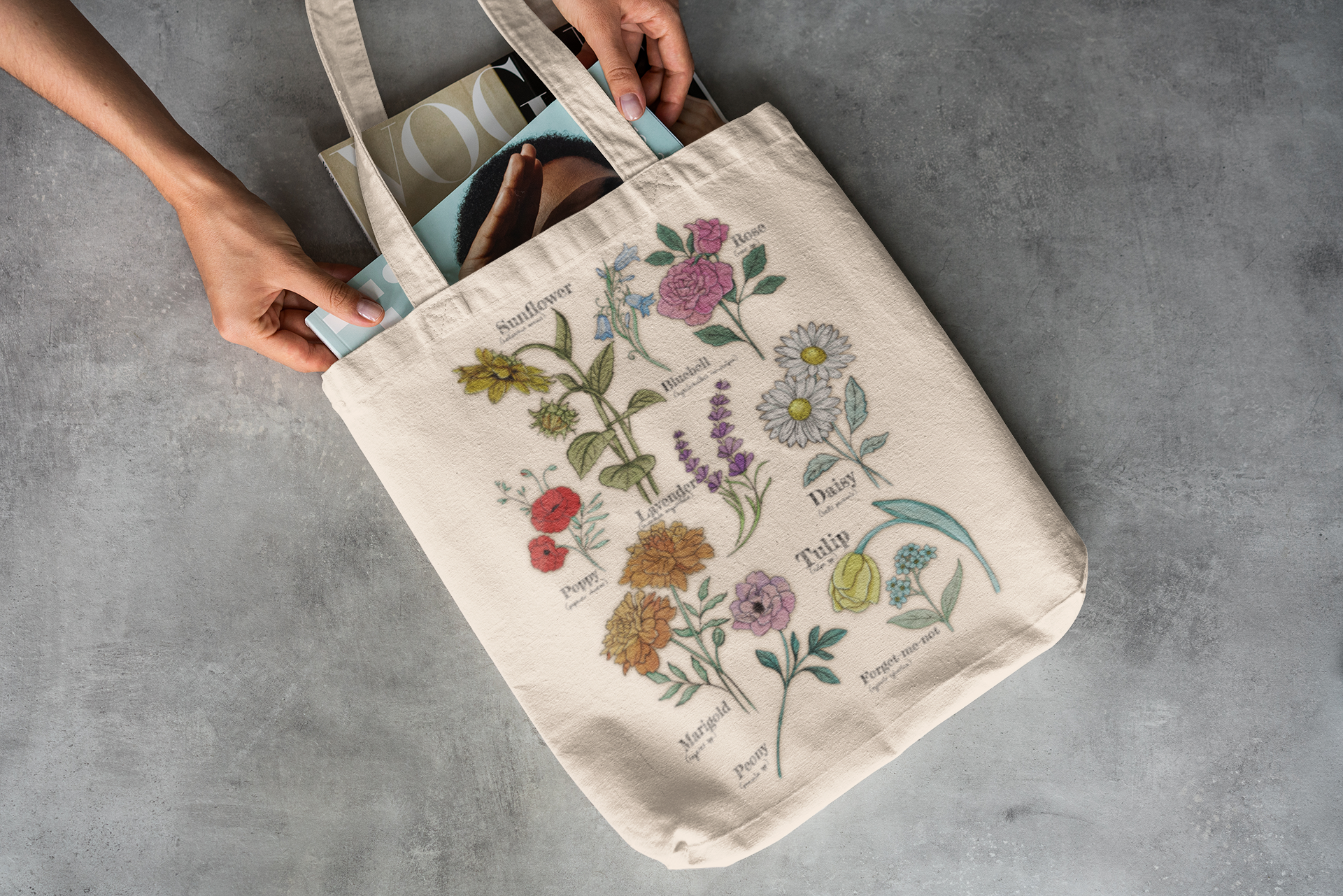 Tote bag with floral designs and text held by a person on a gray surface