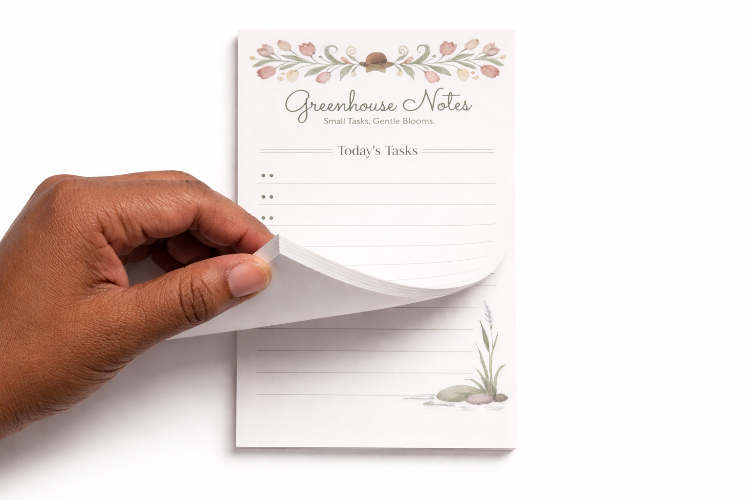 Hand pulling out a sheet from a 'Greenhouse Notes' notepad with floral design on the top.