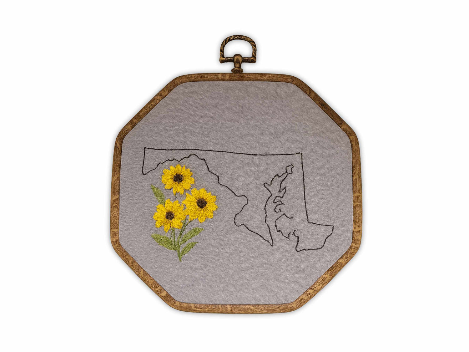 Embroidery hoop art showing Maryland state outline with three yellow black-eyed susan flowers hand-stitched on gray linen fabric