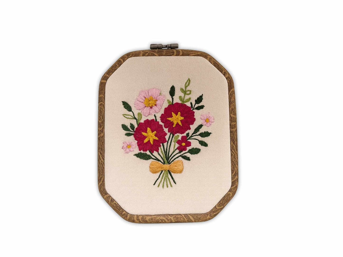 Handmade embroidery hoop art featuring pink and burgundy wildflowers with green leaves tied with golden bow on natural linen fabric in wooden hoop