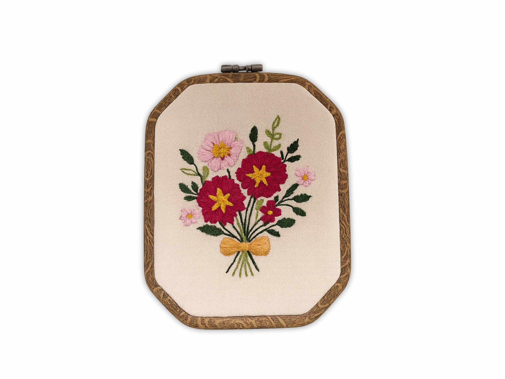 Handmade embroidery hoop art featuring pink and burgundy wildflowers with green leaves tied with golden bow on natural linen fabric in wooden hoop