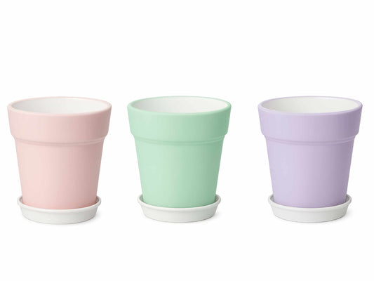 Three plant pots with saucers in soft pastel colors - pink, mint green, and lilac purple - arranged on white background
