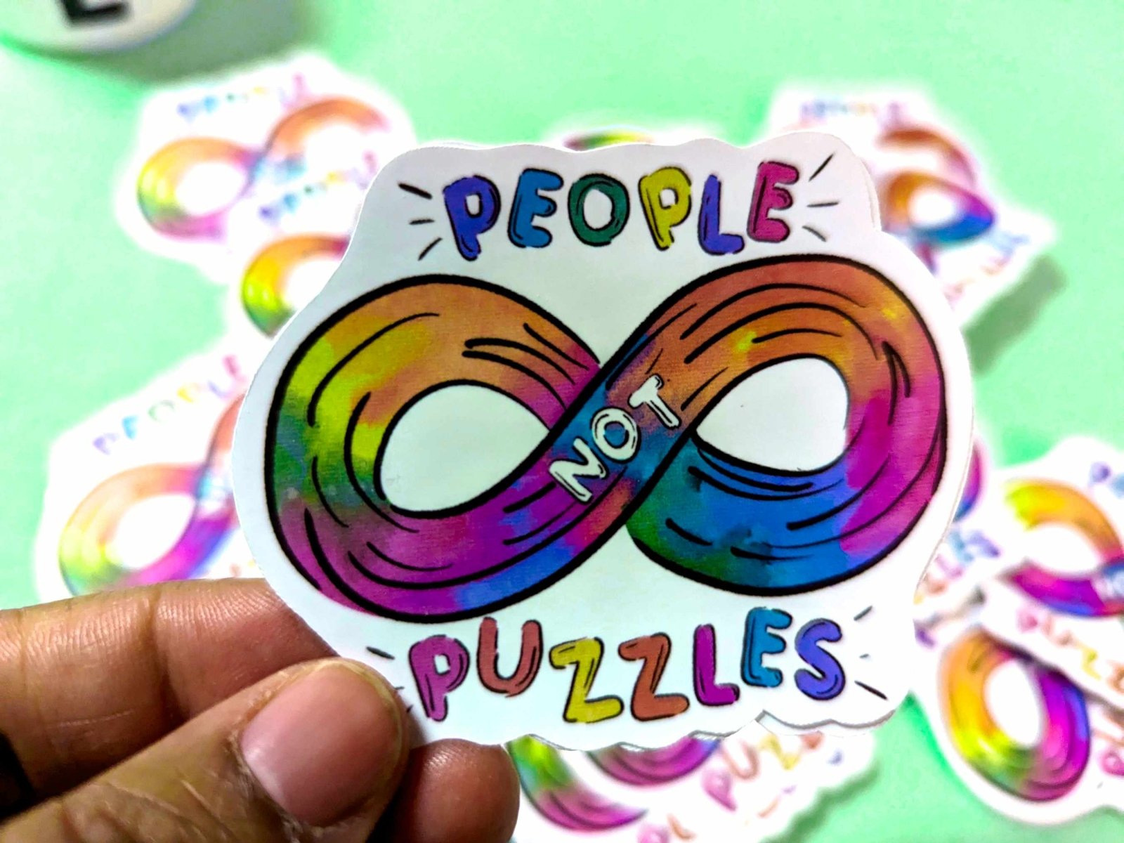 People Not Puzzles Sticker held in hand, featuring a colorful autism infinity sign and waterproof vinyl design