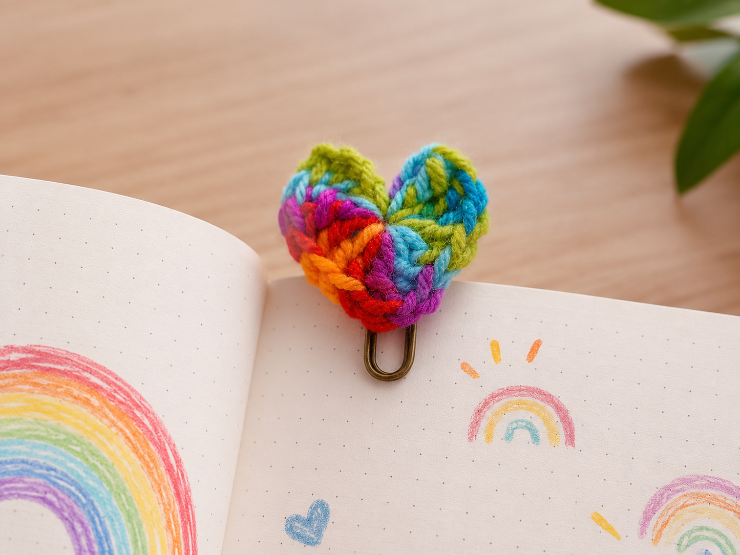 Colorful knitted heart-shaped keychain on an open notebook with rainbow drawings.