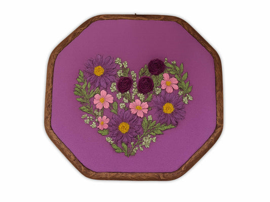 Purple embroidery hoop art with heart-shaped arrangement of burgundy roses, pink cosmos, and purple daisies on rich purple linen fabric