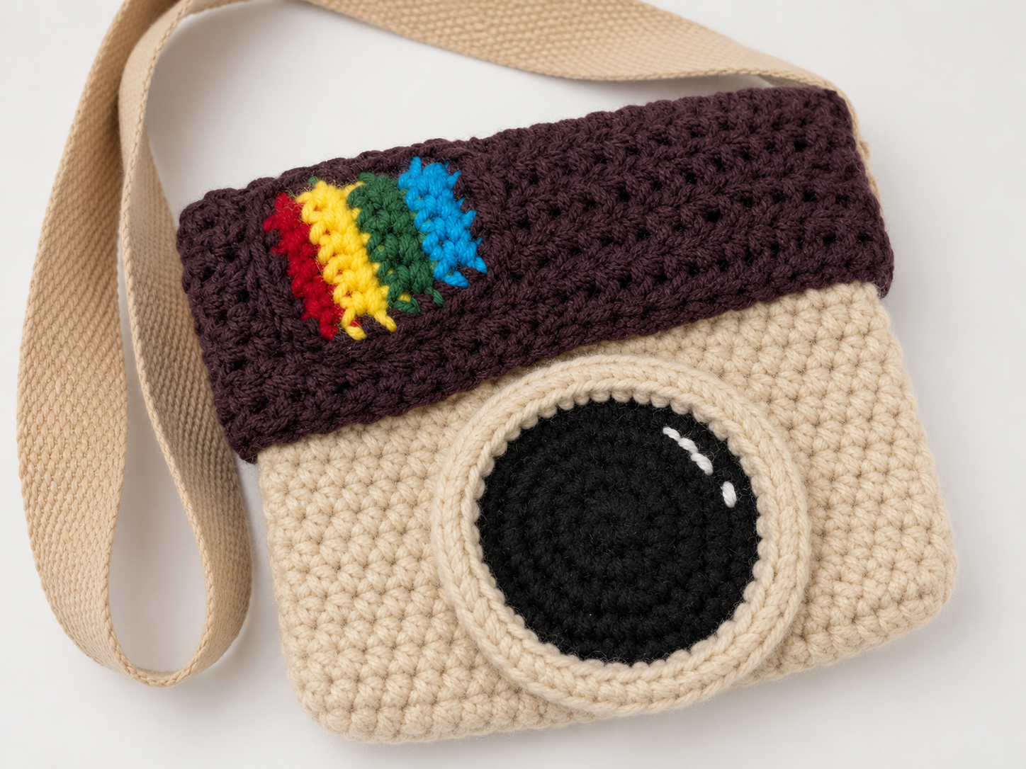 Crocheted camera-shaped bag with rainbow flag on a white background