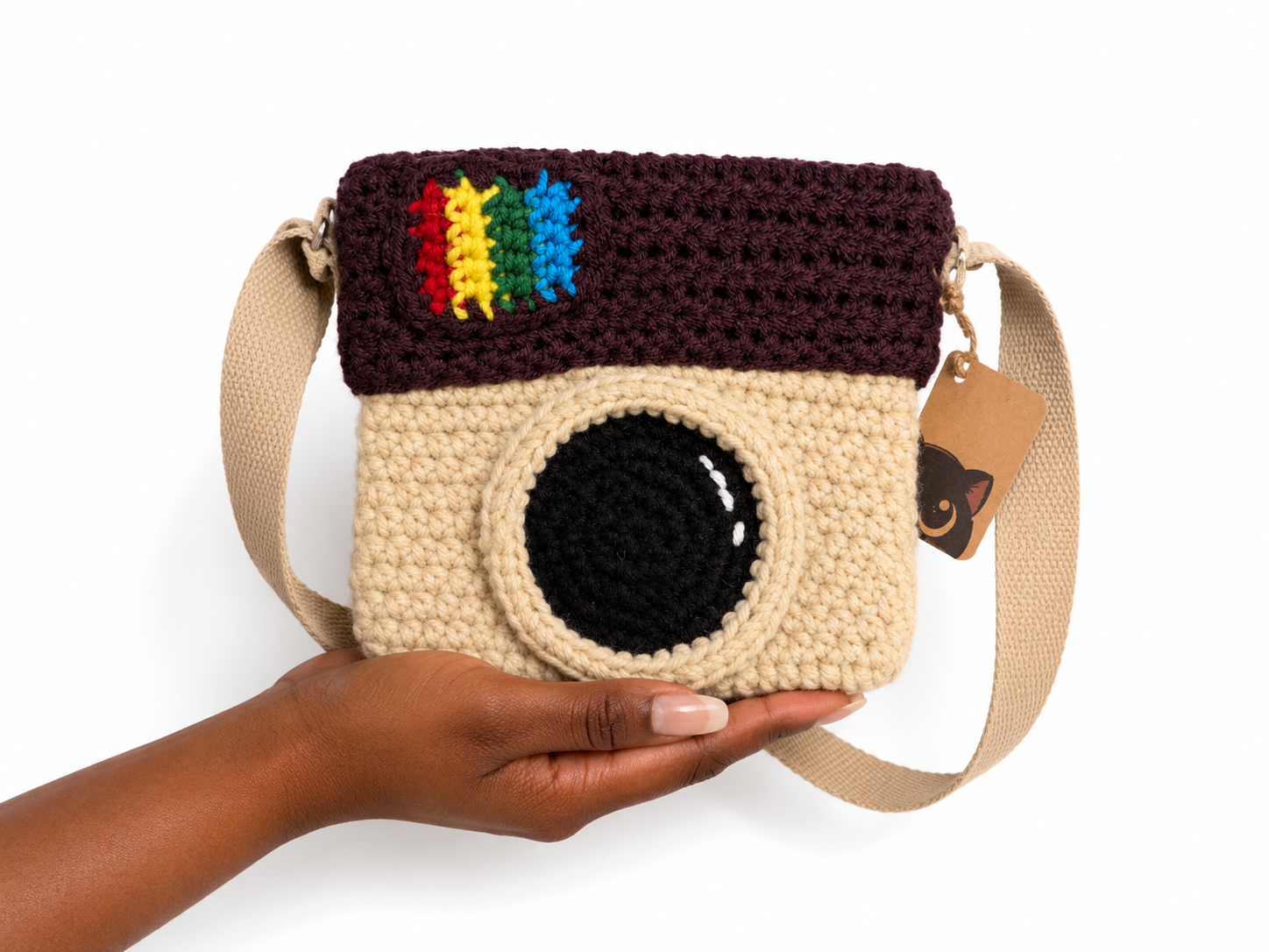 Handmade crochet camera bag with rainbow design held by a person on a white background